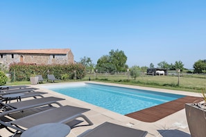Una piscina con lettini, un edificio in pietra e un'area recintata con vegetazione.