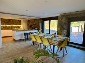 Eine moderne Küche mit Wandverkleidung aus Stein, einem Essbereich mit gelben Stühlen und einer karierten Tischdecke sowie Blick auf einen Innenhof.