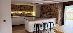 Eine moderne Küche mit Steinrückwand, einer integrierten Kochinsel mit Barhocker und Blick ins Freie.
