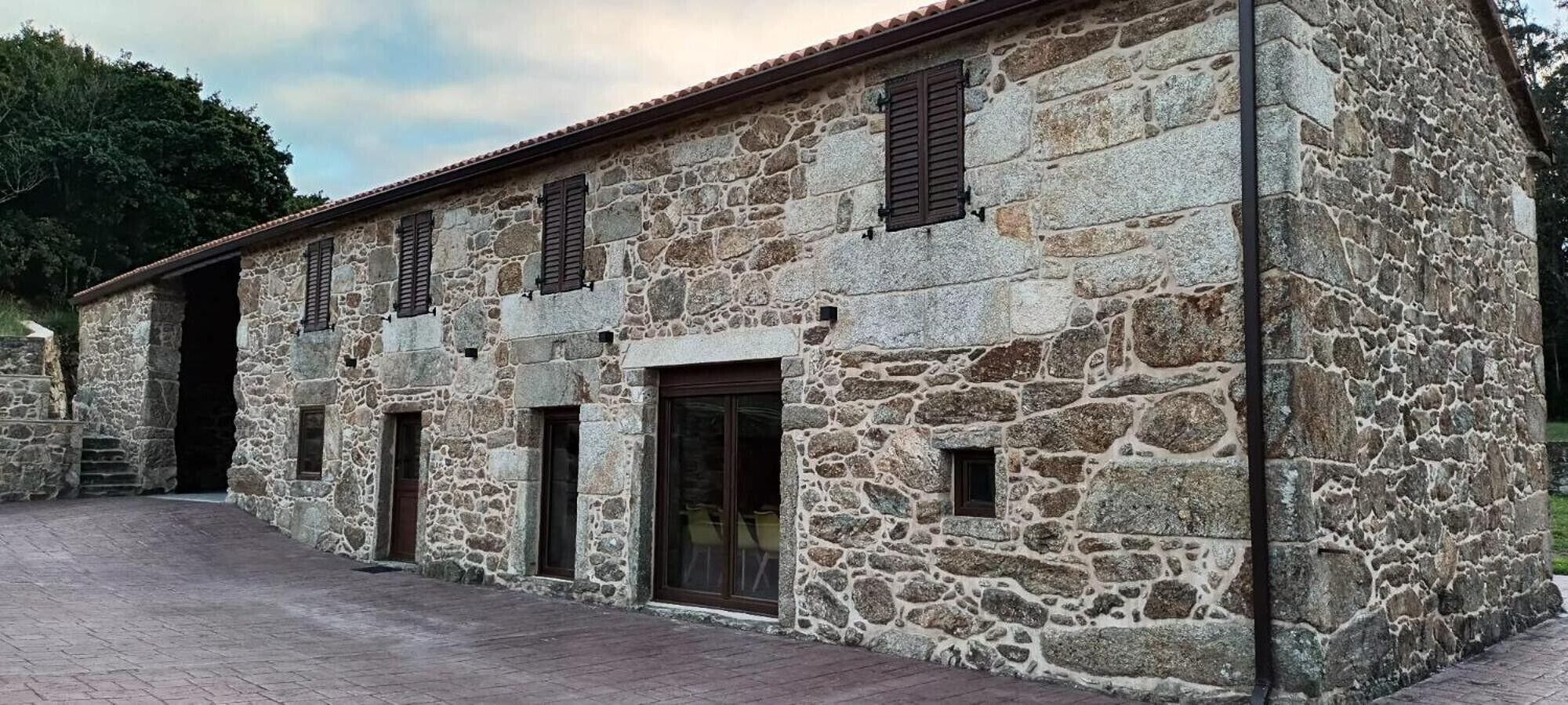 A stone building with multiple windows and doors, a paved entrance, and a stone wall.