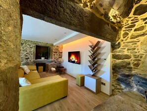 Una habitación con paredes de piedra, una chimenea, un sofá y un televisor.