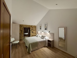 Ein Schlafzimmer mit Stewand, einem Bett mit Kopfteil, einem Nachttisch, einem Spiegel und einem Holzboden.