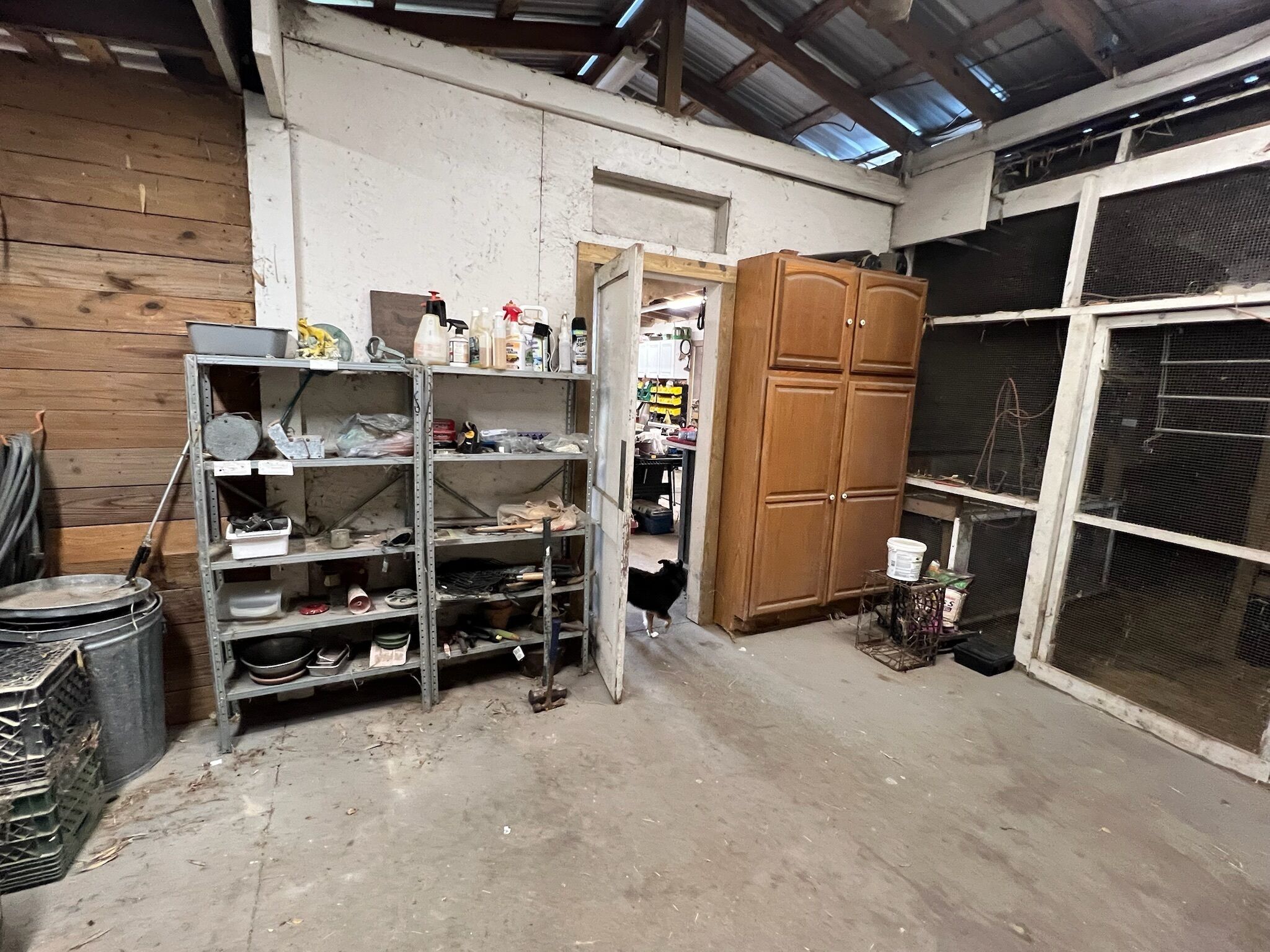 A cluttered storage area with metal shelves, a wooden cabinet, and a large window.