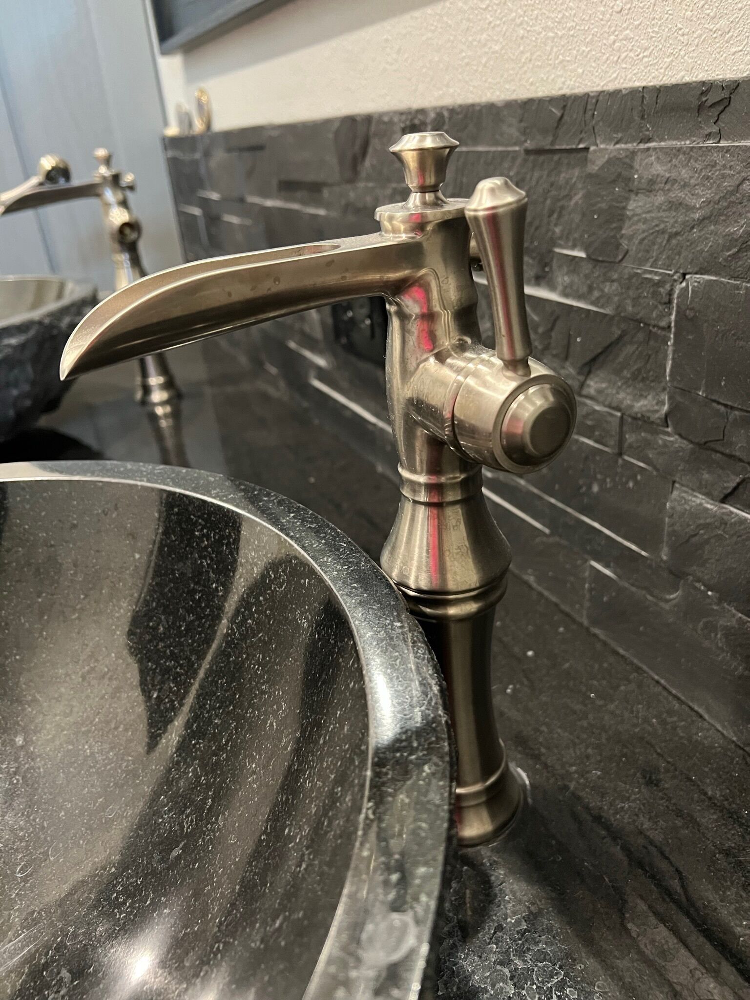 A bathroom sink with a modern faucet and a stone backsplash.