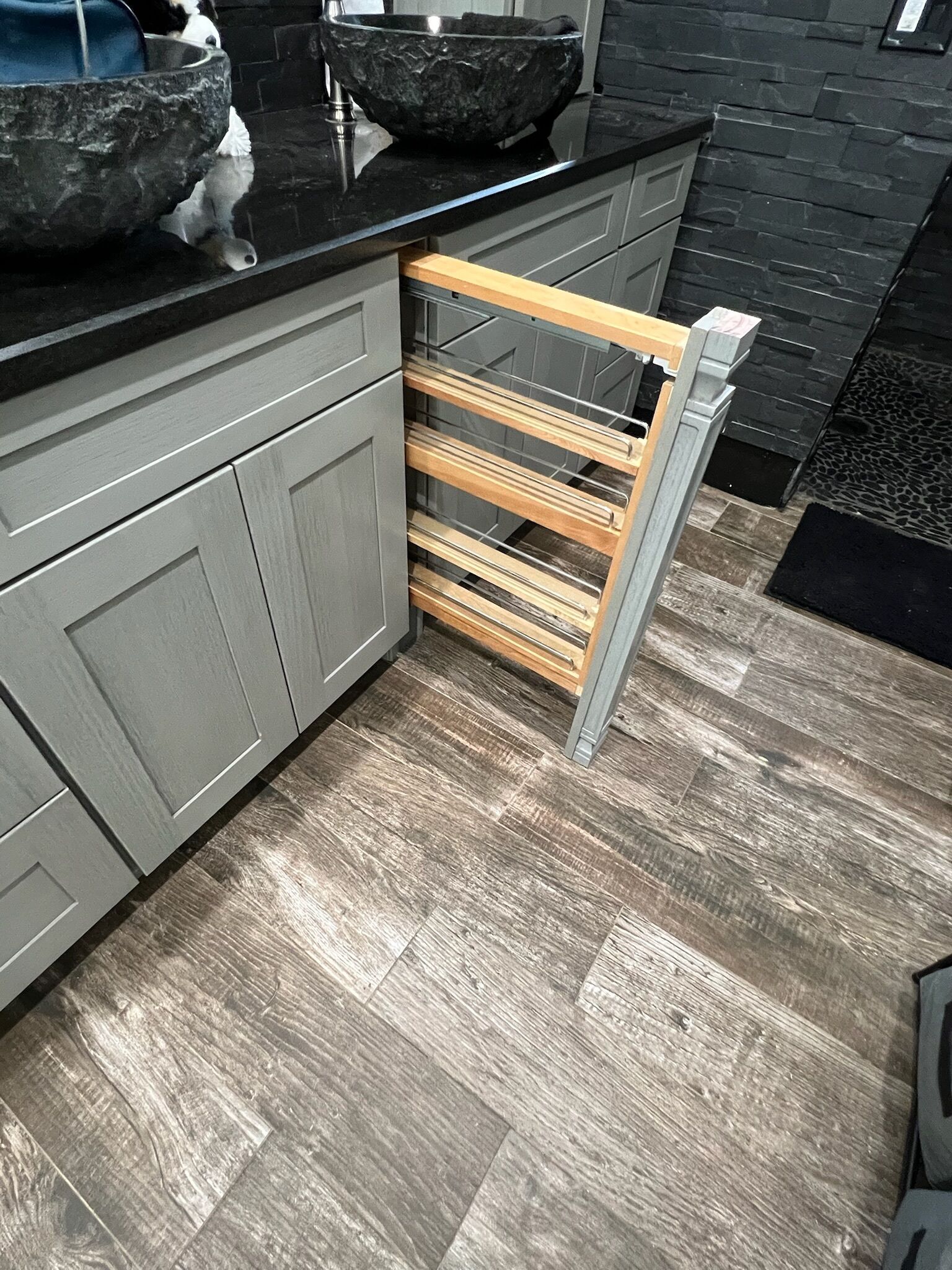 A kitchen with grey cabinets, a black countertop, a stone bowl, and a wooden rack.