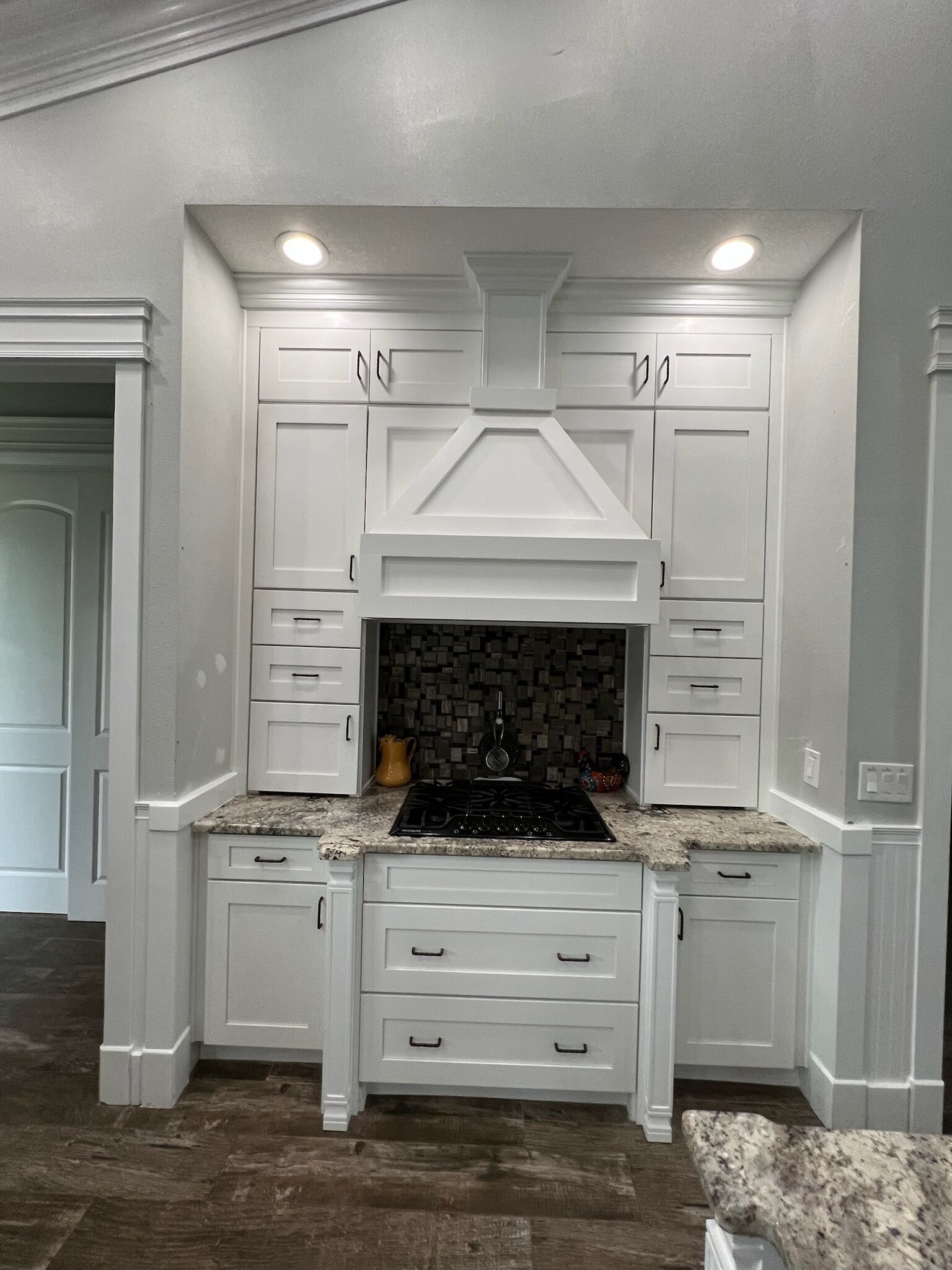 Una cocina con armarios blancos, encimeras de granito, estufa negra y salpicadero de azulejos.
