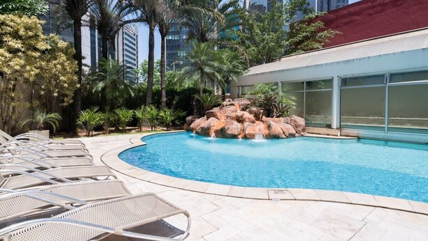 A swimming pool with lounge chairs, palm trees, and a building in the background. - #RD802 | Cyclinn Vila Olímpia (Vila Olímpia)
