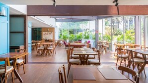 A spacious indoor dining area with wooden tables and chairs, large windows offering a view of greenery outside. - #RD802 | Cyclinn Vila Olímpia (Vila Olímpia)