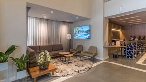 A modern hotel lobby with a sofa, chairs, a coffee table, a TV, and a reception desk. - #TR410 | Cyclinn Faria Lima Itaim (Itaim Bibi)