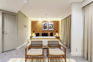 A hotel room with a bed, two bedside tables, a nightstand, two wicker chairs, a large window with curtains, and a wooden headboard with artwork. - #RD513 | Cyclinn Vila Olímpia (Vila Olímpia)