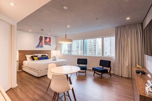 Une chambre d’hôtel moderne, équipée d’un lit, d’une table à manger, de deux chaises, d’un bureau et d’une grande fenêtre avec des rideaux.