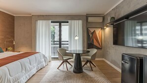 Quarto de hotel moderno com cama, mesa redonda com cadeiras, televisão e vista para o exterior.