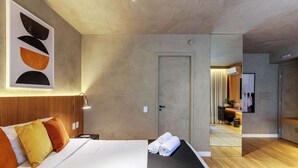 A modern hotel room with a bed, pillows, a wall-mounted artwork, a bedside table, and a neatly made bed with rolled towels. - #RB1107 | Cyclinn Cidade Jardim Itaim (Itaim Bibi)