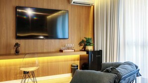 A modern living room with a flat-screen TV mounted on a wooden wall, a sofa, a small table with a vase and glasses, and a black cabinet. - #RB1107 | Cyclinn Cidade Jardim Itaim (Itaim Bibi)