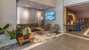 A modern hotel lobby with a sofa, chairs, a coffee table, a TV, and a reception desk. - #TR1209 | Cyclinn Faria Lima Itaim (Itaim Bibi)