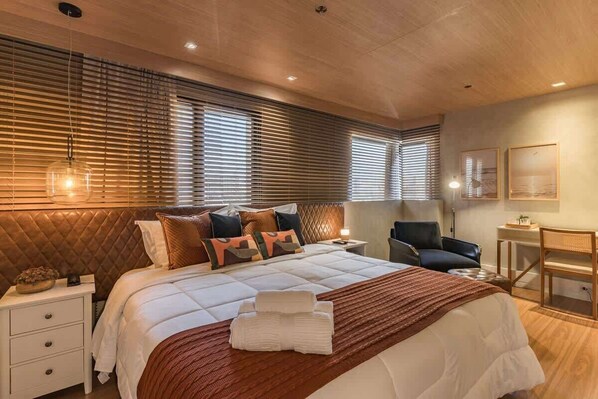 A modern hotel room with a large bed, a desk, a chair, and a window with blinds. - #TR1209 | Cyclinn Faria Lima Itaim (Itaim Bibi)