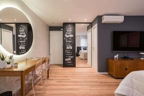 Ein modernes Schlafzimmer mit Fernseher, einer Holzkommode und einer Essecke mit Tisch und Stühlen.