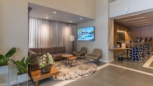 A modern hotel lobby with a sofa, chairs, a coffee table, a TV, and a reception desk. - #TR1204 | Cyclinn Faria Lima Itaim (Itaim Bibi)