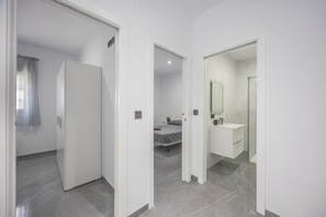 Una habitación de hotel moderna con una cama, un baño con un espejo y lavamanos, y un armario.