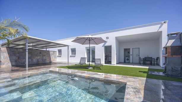 Une maison moderne dotée d’une piscine, de mobilier de jardin et d’un espace extérieur couvert.