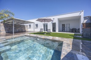 Une maison moderne dotée d’une piscine, de mobilier de jardin et d’un espace extérieur couvert.