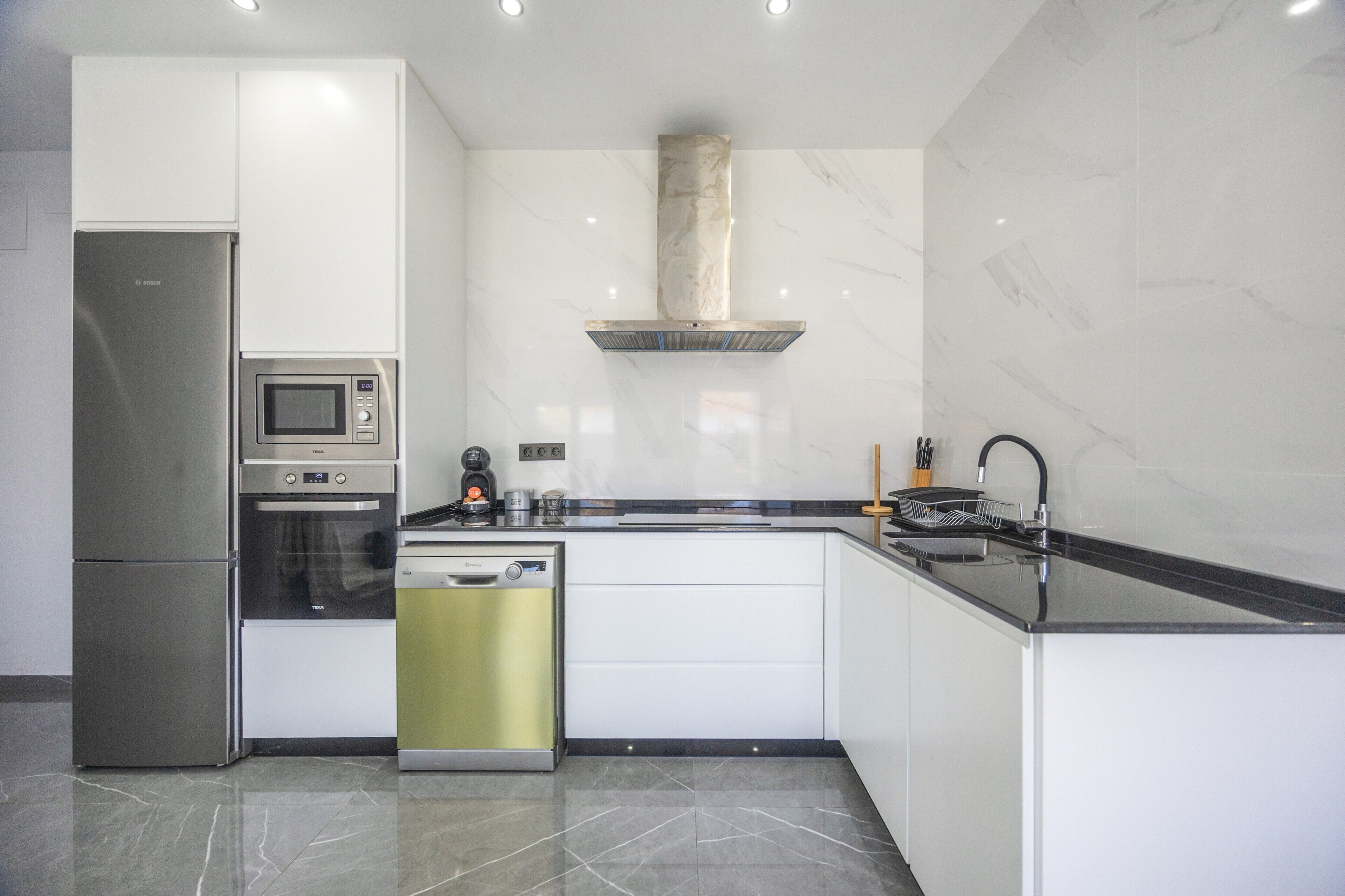 A modern kitchen with a built-in microwave, oven, and dishwasher, a stainless steel refrigerator, and a black countertop.