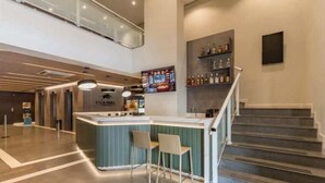 Un espace bar moderne avec un comptoir, deux chaises et un escalier menant à un niveau supérieur.