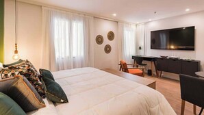 Et moderne hotelværelse med en stor seng, et skrivebord, en stol, et fjernsyn og dekorativ vægkunst.