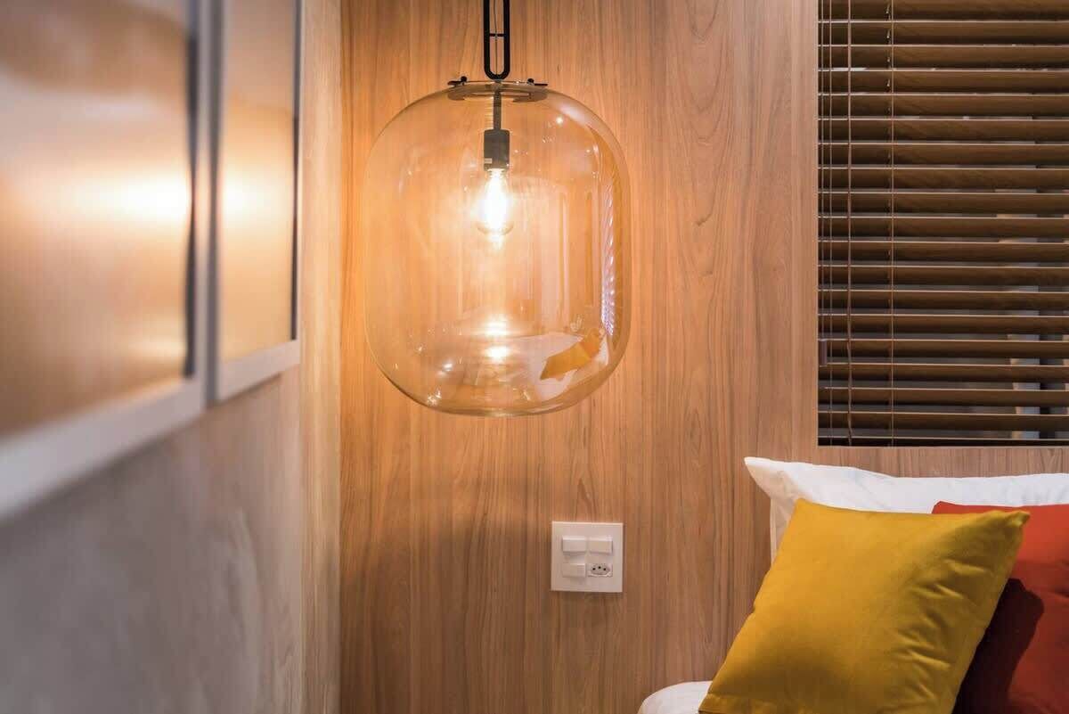 Een kamer met een houten wand, een hanglamp en een bed met kussens.