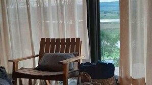 Una habitació amb una cadira de fusta, un sofà i vistes a través de cortines lleugeres.