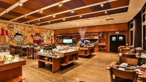 Un restaurant avec des tables et des chaises en bois, une fresque murale et un comptoir où sont exposés des plats.