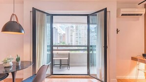 Un appartement moderne doté d’un balcon, d’un coin repas avec une table et des chaises, et d’une grande fenêtre offrant une vue sur la ville.