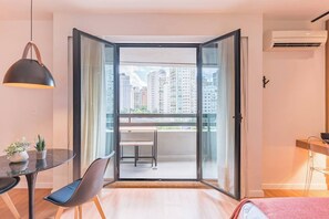 A modern apartment with a balcony, a dining area with a table and chairs, and a large window offering a city view. - #RB406 | Cyclinn Cidade Jardim Itaim (Itaim Bibi)