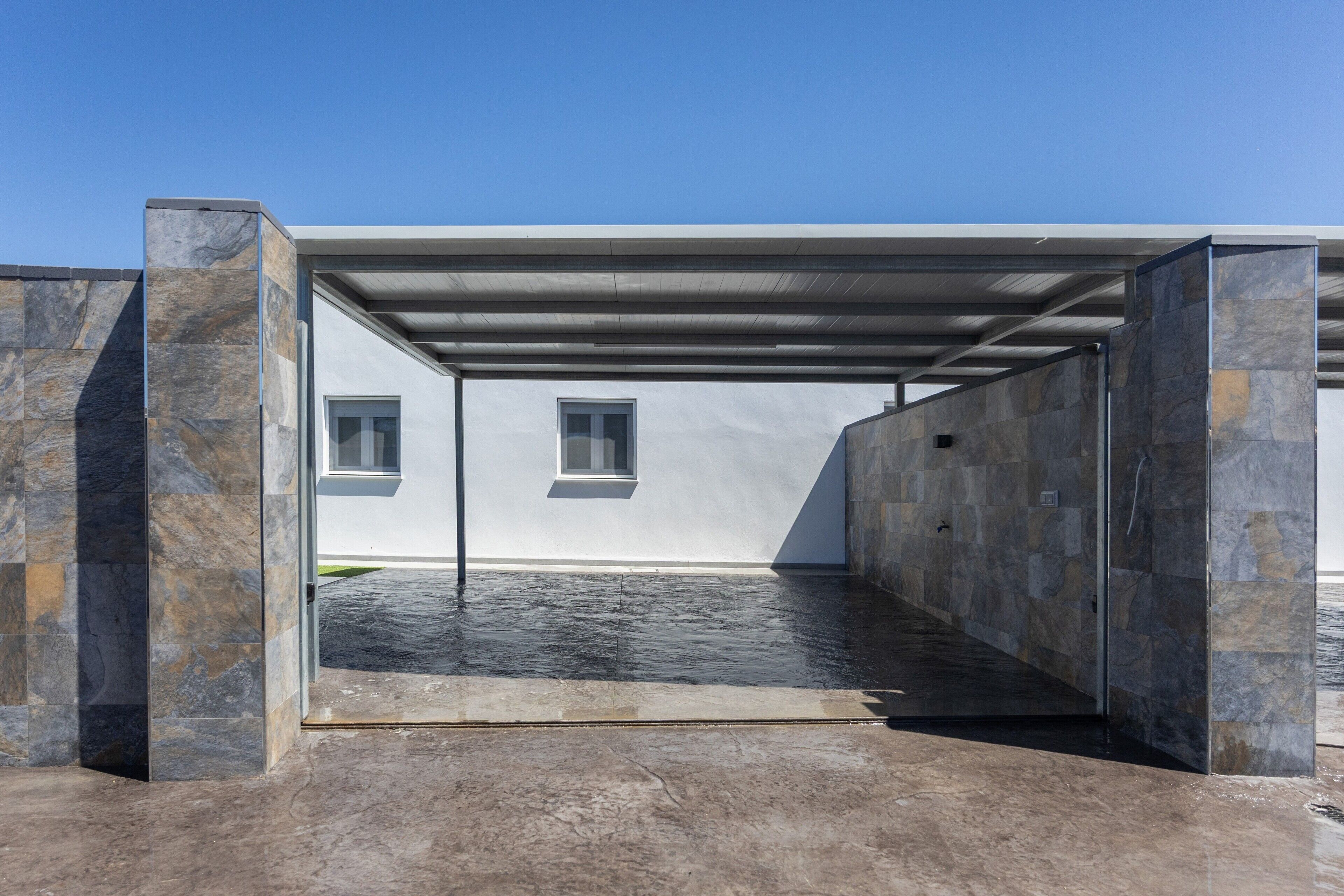 A modern building with a covered outdoor area, stone walls, and a window.