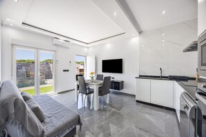 Eine moderne Küche mit Flachbildfernseher, einem Essbereich mit Tisch und Stühlen sowie einem grauen Sofa.