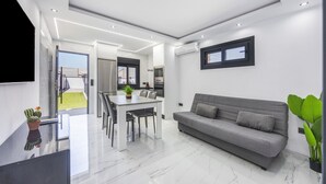Ein modernes Wohnzimmer mit einem grauen Sofa, einem Esstisch mit Stühlen und einem an der Wand befestigten Fernseher.