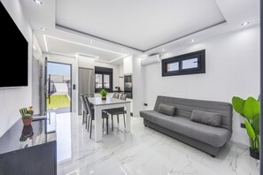 Ein modernes Wohnzimmer mit einem grauen Sofa, einem Esstisch mit Stühlen und einem an der Wand befestigten Fernseher.