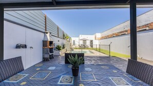 Eine Außenpatio mit gemustertem Boden, einer Sitzecke, einem Topfpflanzen und Blick auf einen Pool und Gebäude im Hintergrund.