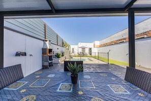 Eine Außenpatio mit gemustertem Boden, einer Sitzecke, einem Topfpflanzen und Blick auf einen Pool und Gebäude im Hintergrund.