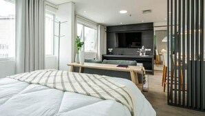 Una camera d'albergo moderna con un letto grande, un'area salotto, una TV a schermo piatto e vista sulla città.