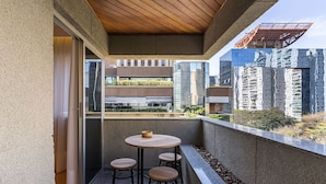 Uma varanda com mesa redonda e quatro banquinhos, teto de madeira e vista para edifícios modernos.