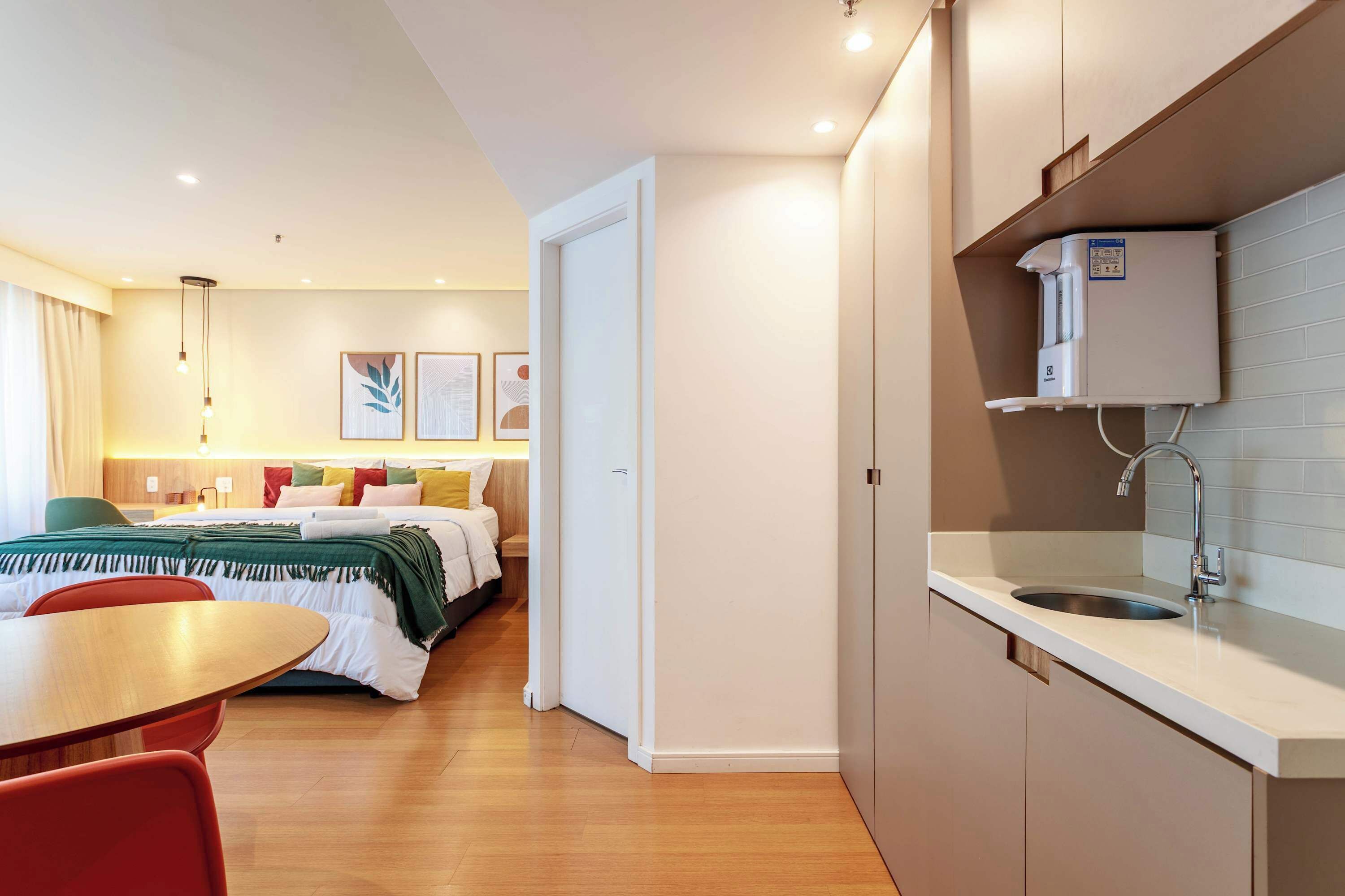 Ein Hotelzimmer mit einem Bett, einem Nachttisch und einer Küchenzeile mit Spüle und Wasserspender.