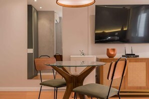 A modern dining area with a glass table, two chairs, a television mounted on the wall, and a wooden cabinet. - #TR1006 | Cyclinn Faria Lima Itaim (Itaim Bibi)