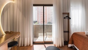 Ein Hotelzimmer mit Schreibtisch, Stuhl, Bett und Blick durch eine Schiebetür auf einen Balkon.