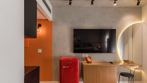Ein moderner Wohnraum mit Flachbildfernseher an der Wand, einem roten PHILCO Kühlschrank, einer Holzbar und einem schwarzen Stuhl.