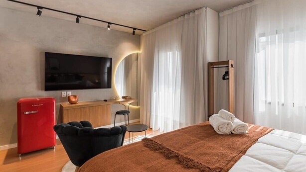 Ein modernes Hotelzimmer mit Bett, Fernseher, Schreibtisch, Sessel und einem roten Gerät.