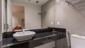 Ein modernes Badezimmer mit einem großen weißen Waschbecken, einer schwarzen Arbeitsplatte, einer Glasdusche und einer sichtbaren Toilette.