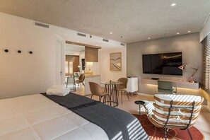 Ein modernes Hotelzimmer mit einem großen Bett, einem Schreibtisch, einem Fernseher und einer Sitzecke mit Sessel und kleinem Tisch.