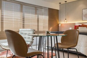 Ein modernes Zimmer mit einem Glastisch, zwei Stühlen, einer gesteppten Couch und einem Bett mit Kopfteil.