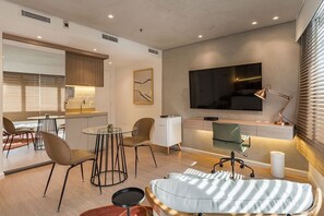 Ein modernes Wohnzimmer mit einer Couch, Sesseln, einem Fernseher und einer Küchenzeile.